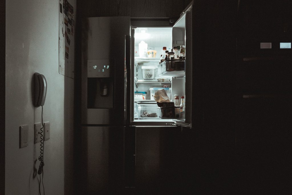 Cameră întunecată cu un frigider deschis în care se află alimente.