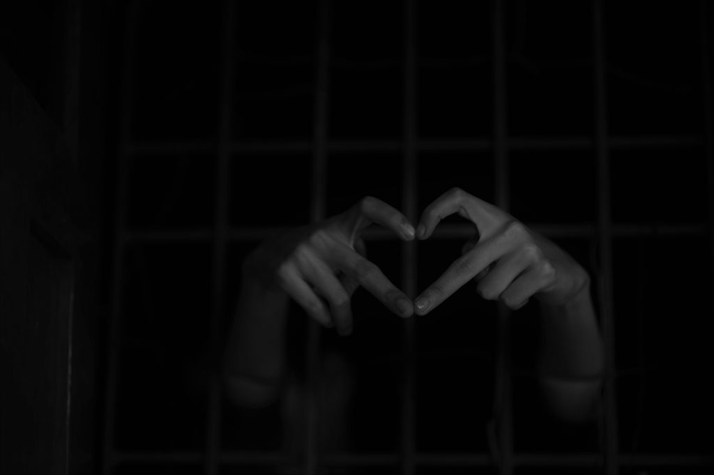 Două mâini care formează o inimă din degete printre gratiile unei celule din închisoare