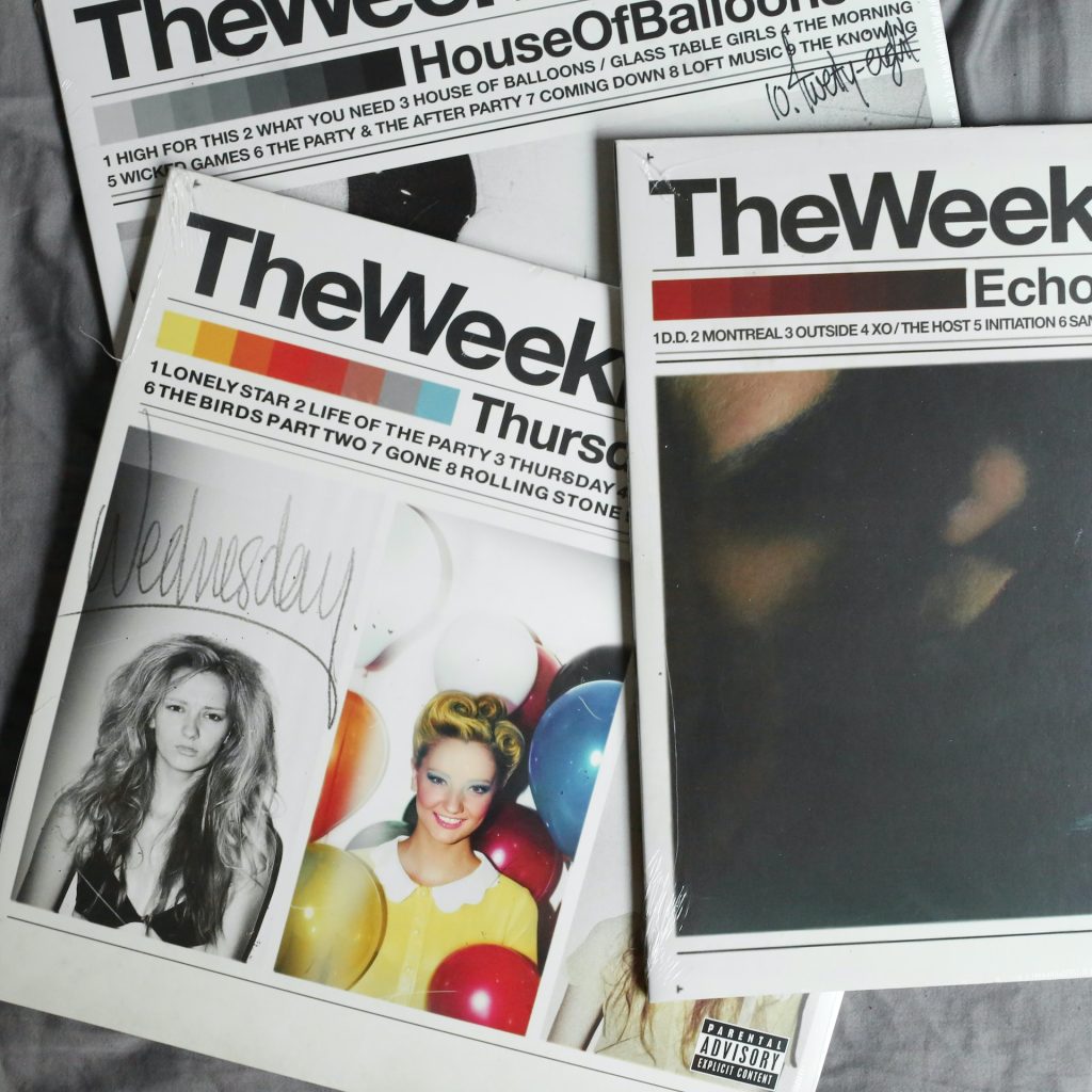 CD-uri ale artistului The Weeknd, așezate una peste alta pe o masă.